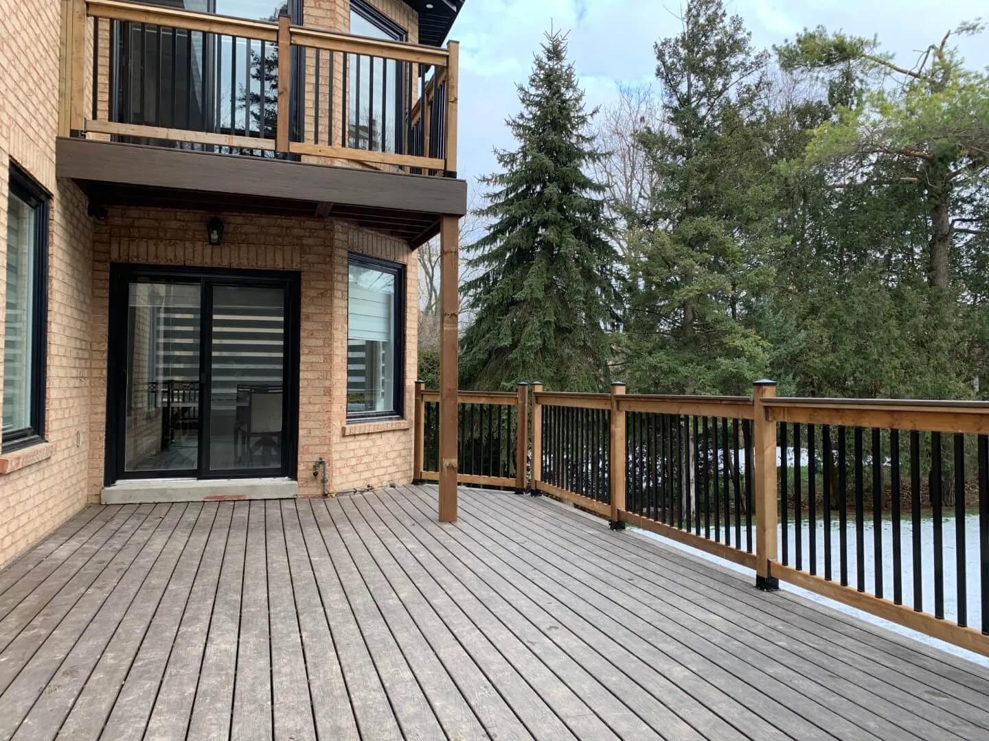 Wood deck with black metal railing beside a brick home
